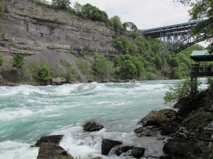 rushing water from a rocky shore, a bridge spans the river in the background